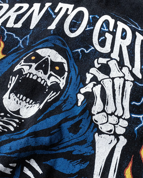 Close up of a vintage wash black shirt with a screen printed graphic of a skeleton grilling a steak on a BBQ. The skeleton chef wears a blue apron that says ‘Kill the Cook’ and is surrounded by yellow flames and lue lightning. Text reads ‘Born To Grill’. Skeleton chef, steak, chef tee, chef shirt